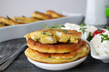 Fritters with fresh green onion and pieces of boiled egg on a white plate with fresh greek yoghurt on a dark wooden background. Healthy breakfast. Healthy eating concept