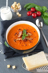 Thick tomato soup with basil and fried bacon in a black ceramic bowl on a grey abstract background. Healthy eating concept Fresh tomato soup with creme fraiche