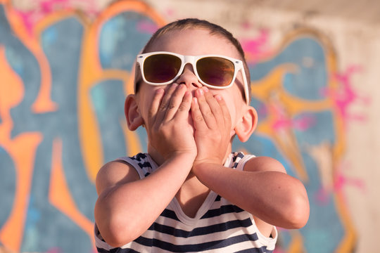happy little boy wearing sunglasses closed his mouth with hands