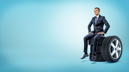 A serious businessman sitting on a stack of car tires with hands on his hips. © gearstd