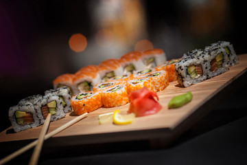Appetizing rolls lie on a wooden plate. Traditional serving. Wasabi, lemon. The atmosphere is warm, cozy restaurant. Creative color.