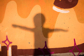 Silhouette of boy placing his hands in flight against background of graffiti wall