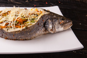 Fish with filling, stuffed with vegetables and cheese on white plate. Close-up