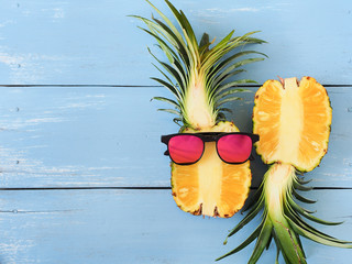 Ripe fresh pineapple and sunglasses on blue wooden table.