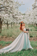 Fototapeta premium Young red-haired woman in a luxurious dress is standing in a blooming garden