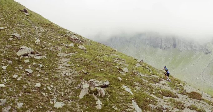 aerial flight above caucasian trail runner running to mountain through rocky climb.wild green nature outdoors in cloudy and foggy weather. 4k drone side wide passthrough video