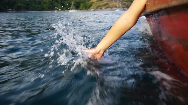 Female hand touches the surface of the sea sailing in a boat. Slow motion