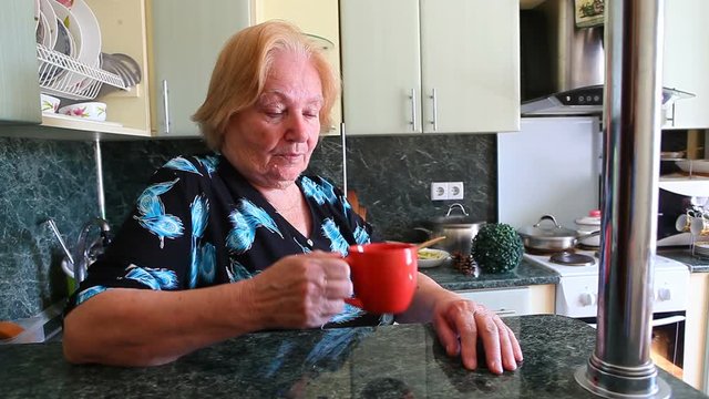 Old woman drinking cup of tea and smiling on the kitchen