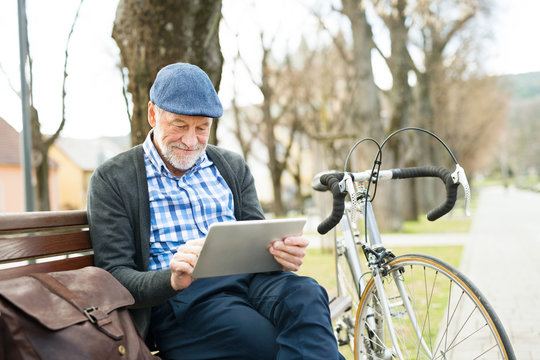 Senior man in town sitting on bench, working on tablet