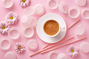 Flat lay coffee cup with cupcake papers and flowers. Pink pastel background. Top view.