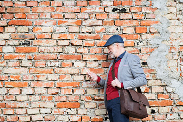 Fototapeta na wymiar Senior man with smartphone against brick wall, texting.
