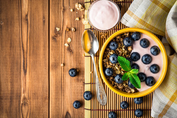 Granola with blueberries and yogurt in yellow bowl on wooden table.