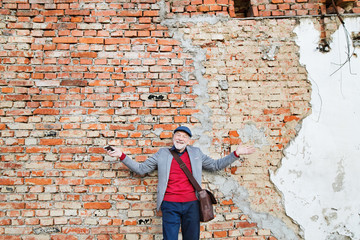 Senior man with smartphone against brick wall.
