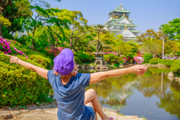 Naklejka premium Szczęśliwy turysta cieszy się przed Zamkiem Osaka otoczonym wiosennymi kwiatami. Koncepcja podróży wolności i Azji. Niewyraźne tło. Zamek Osaka to jeden z najbardziej znanych zabytków w Japonii i Osace.