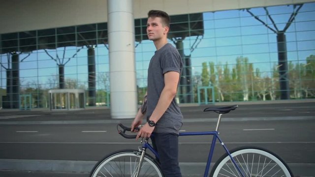 Handsome man standing and holding his bicycle near the airport slow motion