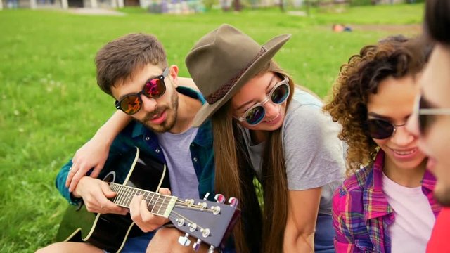 Group of young handsome people at picnic, while they plays guitar and sings. Friends at summer concept. Close up shot at steadicam