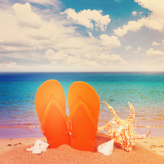 pair of orange flip flop sandals in sand on the beach near sea water, retro toned