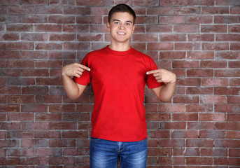 Handsome young man in blank red t-shirt standing against brick wall