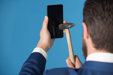 man cracks smartphone with hammer, broken phone on blue background