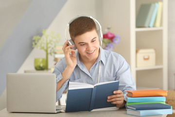 Young man sitting at table and listening to audio book