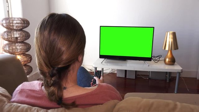 Girl changing Channels On Green Screened Television. Young Woman watching television with green screen, shot behind models shoulders