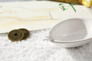 Acupuncture needles in bowl and coins on towel
