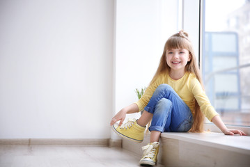 Little fashion girl sitting on window sill in light room