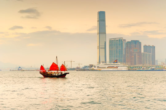 Hong Kong skyline with a red Chinese sailboat passing on the Victoria Harbor at dusk