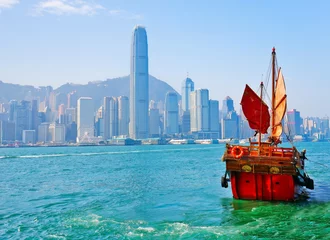 Foto op Canvas View of Hong Kong skyline with a red Chinese sailboat passing on the Victoria Harbor in a sunny day. © Javen