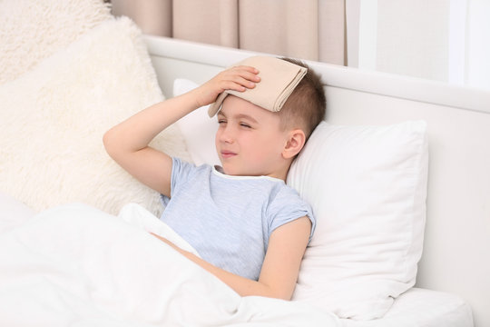 Little boy suffering from headache while lying in bed with compress