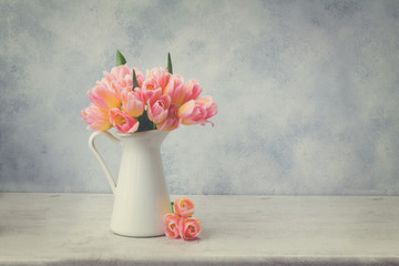 fresh pink and yellow tulips in white vase on gray background, retro toned