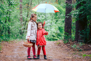 two beautiful sisters are hiding from the rain under one umbrella color in the woods