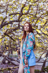 Portrait of young beautiful woman posing among blooming trees with pink eyeshadow. Spring look on magnolias background. posing and looking at camera.