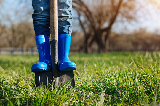 Close up of childs feet in rubber boots on shovel