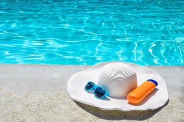 Fototapeta na wymiar Summer hat, sunglasses and sunscreen near the pool