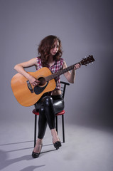 Young woman plays on an acoustic guitar, isolated on a gray background.