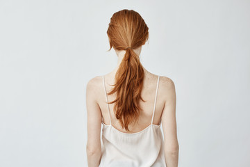 Obraz premium Portrait of young pretty girl with foxy hair posing back to camera over white wall