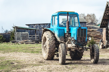 An old tractor front view in the countryside amid barns and sheds.