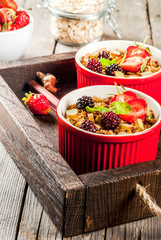 Healthy breakfast. Oatmeal granola crumble with rhubarb, fresh strawberries and blackberries, seeds and ice cream in baked bowls, decorated with mint, on a wooden rustic table in old tray, copy space