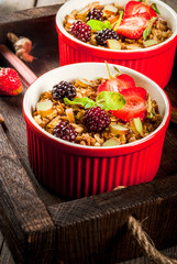 Healthy breakfast. Oatmeal granola crumble with rhubarb, fresh strawberries and blackberries, seeds and ice cream in baked bowls, decorated with mint, on a wooden rustic table in old tray, copy space