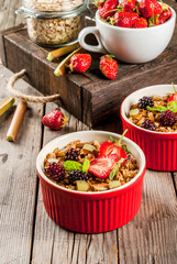 Healthy breakfast. Oatmeal granola crumble with rhubarb, fresh strawberries and blackberries, seeds and ice cream in baked bowls, decorated with mint, on a wooden rustic table in old tray, copy space