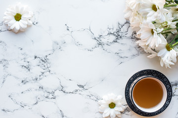 Top view of cup of tea and flowers on white marble background, flat lay - obrazy, fototapety, plakaty
