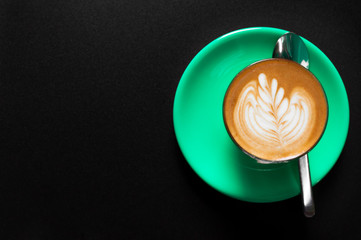Hot latte in green cup with floral pattern in foam top view on a dark background