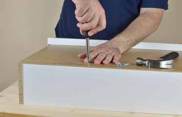 Man's hands screwing a wood screw in a drawer backside set on working table