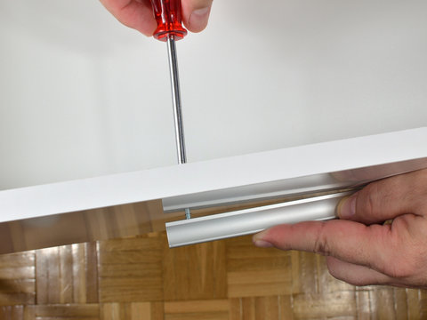 Man's hands screwing a handle in a drawer side 