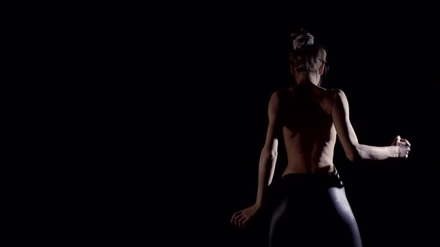 Young sporty girl with Nude back sexy moves in a dark room. Visible ribs on a slender back and the vertebrae.