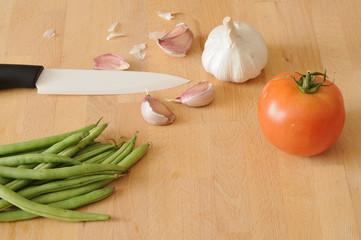 Green beans on a kitchen table, with a ceramic knife, garlic, tomato, top view