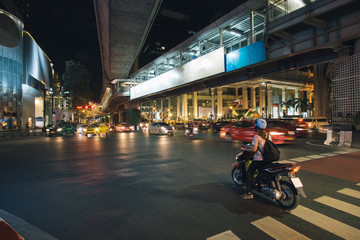 Night city traffic of cars and motorbikes moves slowly along a busy highway road with subway above the road near the city center in Bangkok, Thailand, cityscape photography.