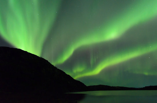 The Aurora in the sky above the hills and the lake.