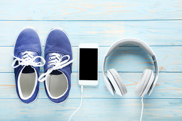 Naklejka premium Sport shoes with smartphone and headphones on blue wooden table